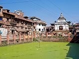 Kathmandu Valley 2 Kirtipur 03 Pond In Village Square, Former Royal Palace, Small Temple A walking tour through the winding streets of Kirtipur near Kathmandu offers a stroll into the past. Cobble stones, charming brick houses, carved wood windows, and inhabitants in homespun attire. The central Kirtipur square across from the entrance to the Bagh Bhairav Temple was the former royal residence, and has a pond with brackish green water and a small temple.